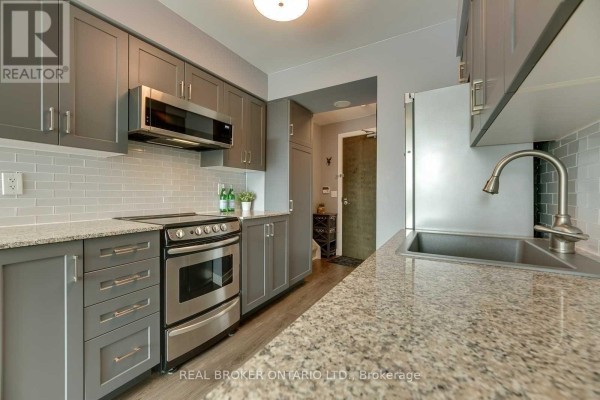 Kitchen layout with stainless steel sink, dishwasher, stove, grey cabinets, granite countertops, and subway tile backsplash. - 407 - 50 Lynn Williams Street, Toronto