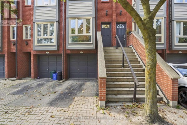 Close-up of townhouse entrances with red brick accents, dark grey doors, and attached garages below. - 407 - 895 Maple Avenue, Burlington