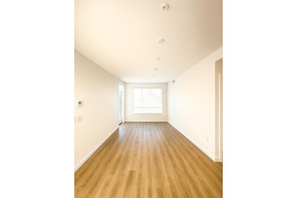 Empty living room with light-colored walls, hardwood floors, and a large window. - 407 27215 Aldergrove Town Centre Drive, Langley