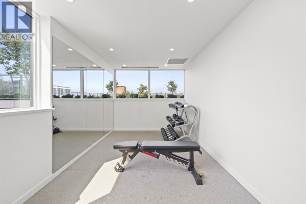 Weightlifting area in a gym with a bench, dumbbells, and mirrored walls reflecting large windows. - 407 8415 Granville Street, Vancouver