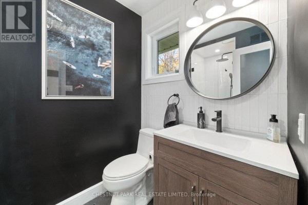 Modern bathroom with wood vanity, round mirror, black accent wall, and artwork - 407 County Road 4 Prince Edward County