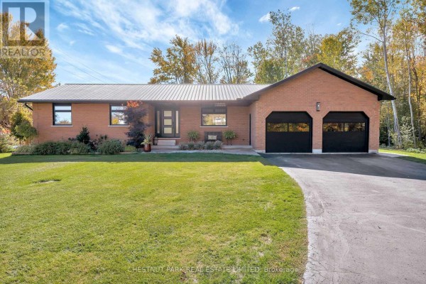 Brick home with metal roof, two-car garage, and modern front door - 407 County Road 4 Prince Edward County