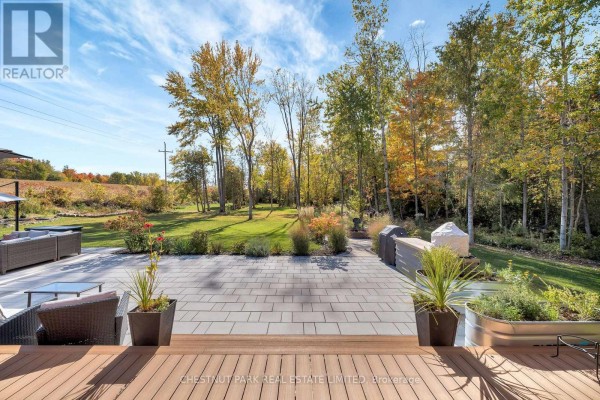 Modern paver patio with outdoor kitchen, grill, and seating overlooking a treed backyard.