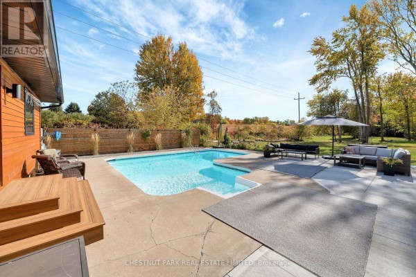 Inground pool with a concrete surround, patio furniture, and surrounding trees. - 407 County Road 4, Prince Edward County