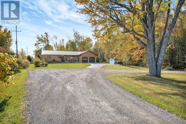 Gravel driveway leads to a brick house with a metal roof and detached shed. - 407 County Road 4, Prince Edward County
