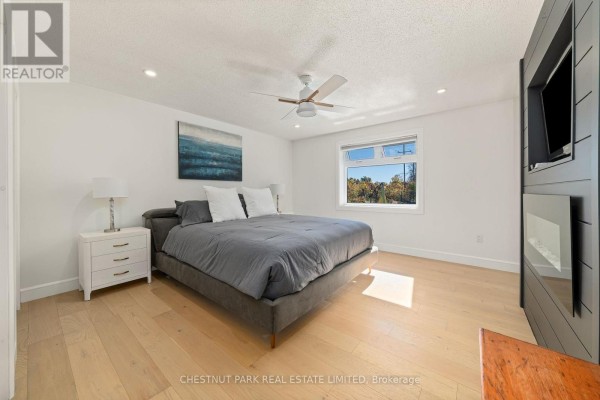 King-size bed with gray comforter, ceiling fan, mounted TV, fireplace, and hardwood floors - 407 County Road 4 Prince Edward County