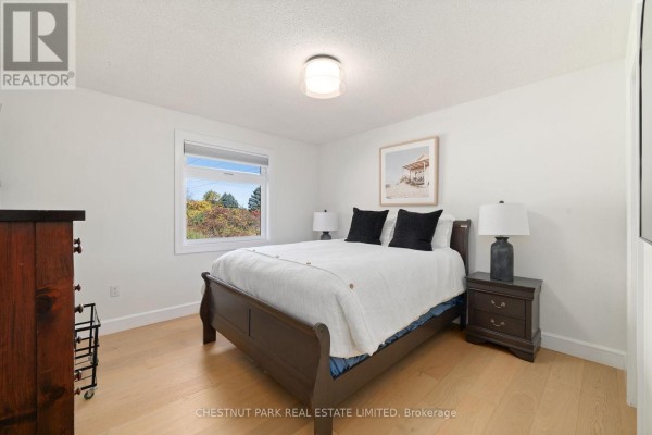 Bedroom with dark wood bed, white bedding, and autumn foliage view - 407 County Road 4 Prince Edward County