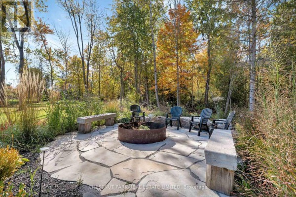 Flagstone patio with fire pit, chairs, and benches surrounded by trees - 407 County Road 4 Prince Edward County