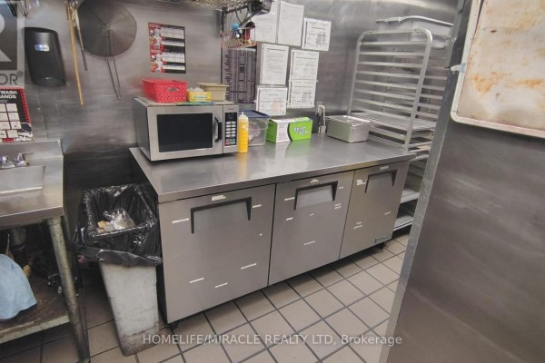 Commercial kitchen with stainless steel counters, microwave, and a trash bin. - 407 Dalhousie Street, Ottawa