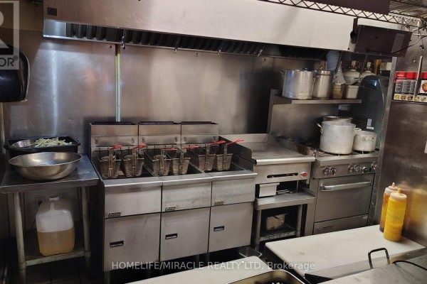 Commercial kitchen with multiple deep fryers, a griddle, stove, and stainless steel shelving. - 407 Dalhousie Street, Ottawa