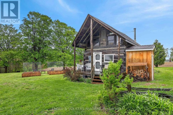 Exterior of a small log cabin with a covered front porch and firewood stacked beside. - 40751 Londesboro Road, Central Huron