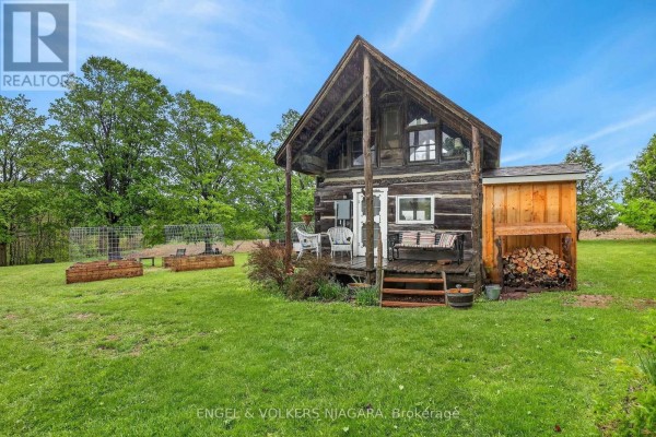Side view of a log cabin with a covered porch, porch swing, and flower beds. - 40751 Londesboro Road, Central Huron