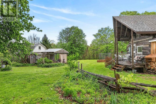 View of a rustic cabin and enclosed porch area from a grassy yard with wooden fencing. - 40751 Londesboro Road, Central Huron