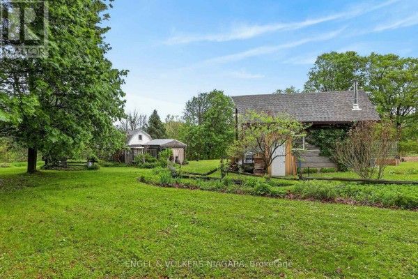 Expansive grassy yard with mature trees, a rustic cabin, and an enclosed sunroom structure. - 40751 Londesboro Road, Central Huron