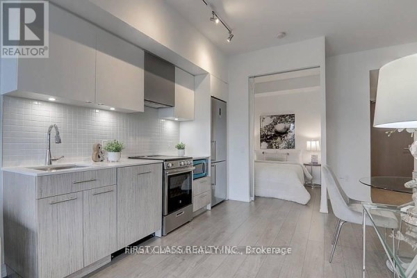 Compact kitchen with light wood cabinets, white tile backsplash, and stainless steel appliances. - 408 - 251 Jarvis Street, Toronto
