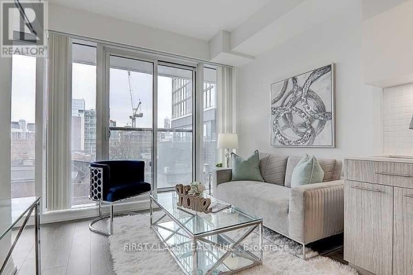 Living area with a grey sofa, blue accent chair, glass coffee table, and large window. - 408 - 251 Jarvis Street, Toronto