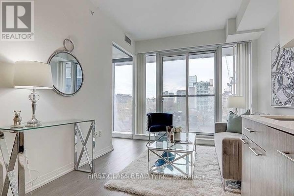 Living room with large windows, a grey sofa, blue chair, and a mirrored console table. - 408 - 251 Jarvis Street, Toronto
