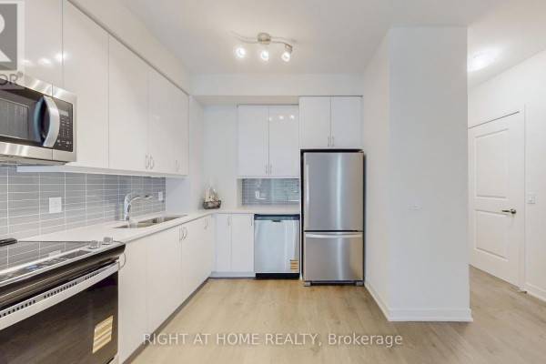 Corner kitchen with stainless steel appliances, white cabinetry, and grey tiled backsplash. - 408 - 38 Annie Craig Drive, Toronto