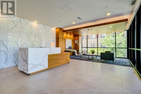 Apartment building lobby featuring a white reception desk, marble accent wall, and seating area. - 408 - 50 Ann Street, Caledon