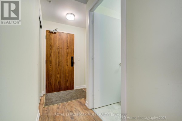 Interior view of an apartment hallway with a wooden door and a light gray rug. - 408 - 50 Ann Street, Caledon