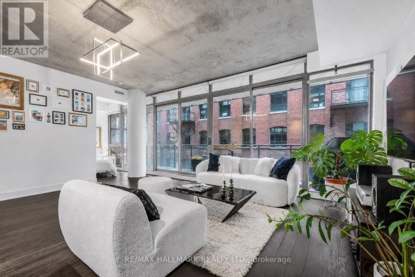Living room with floor-to-ceiling windows, contemporary white sofas, and a view of the brick building opposite. - 408 - 90 Broadview Avenue, Toronto