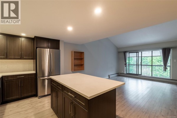 Spacious kitchen view with island, stainless steel fridge, and light wood flooring. - 408 1005 Mckenzie Ave, Saanich