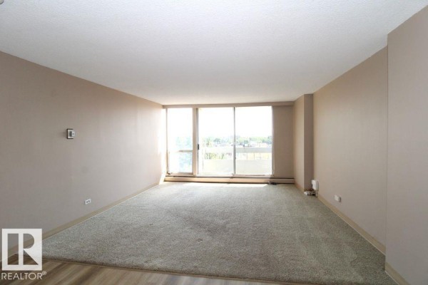 Living room with beige carpet, tan walls, and a large sliding glass door overlooking the city. - #408 10883 Saskatchewan Dr Nw, Edmonton