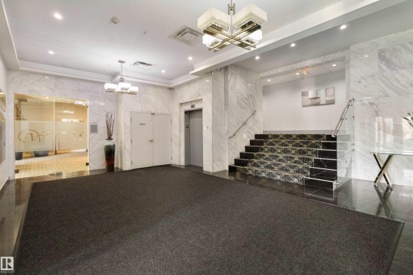 Apartment building lounge area with grey sofas, glass coffee tables, patterned carpet, and large windows. - #408 1350 Windermere Wy Sw, Edmonton