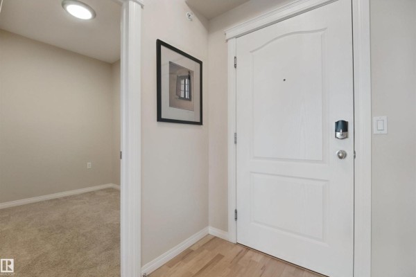 Interior hallway with a closed white door, beige walls, framed picture, and wood floor. - #408 45 Inglewood Dr, St  Albert