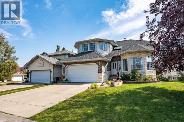 Exterior view of a two-story house with a double garage, light brick, and dark shingles. - 408 Hawkland Place Nw, Calgary