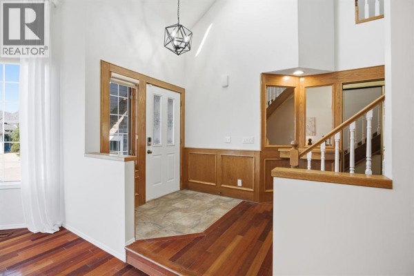 Entrance foyer with white walls, wood trim, tiled floor, and a wooden staircase. - 408 Hawkland Place Nw, Calgary
