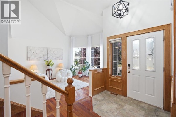 Interior view of a bright foyer with white walls, a wooden staircase, and large windows. - 408 Hawkland Place Nw, Calgary