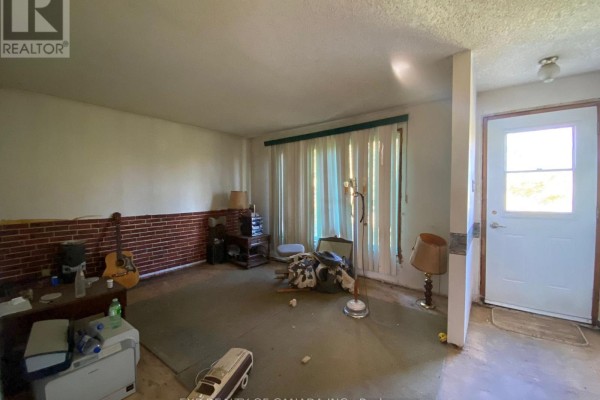 Living room with beige carpet, white walls, a brick accent wall, and a closed white door. - 408 Silver Queen Lake Road, Cochrane