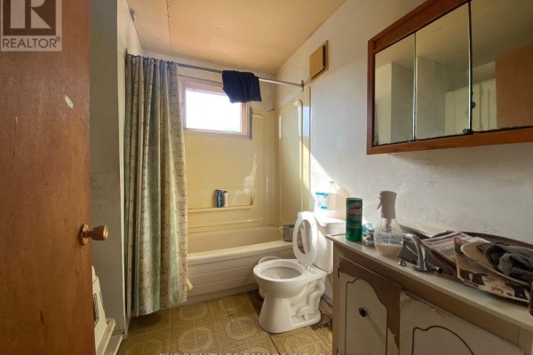 Small bathroom with a bathtub, toilet, vanity, and a window with a patterned shower curtain. - 408 Silver Queen Lake Road, Cochrane