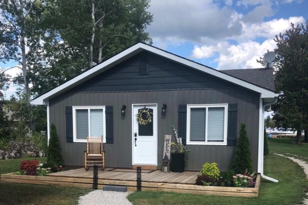 Front facade of a grey vinyl-sided cottage with a wooden porch. - 4089 Glen Cedar Drive, Ramara