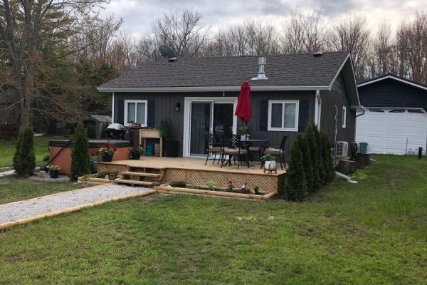 Rear view of a cottage with a deck, hot tub, and garage. - 4089 Glen Cedar Drive, Ramara