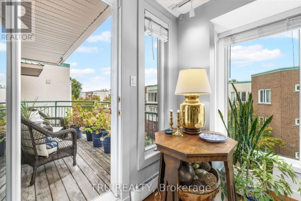 Interior corner with a wooden table, lamp, and plants, looking out to a balcony. - 408a - 62 Donald Street, Ottawa