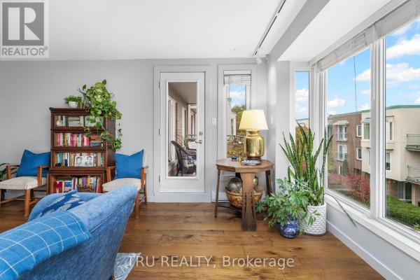 Living area with a blue sofa, bookshelves, and large windows overlooking the courtyard. - 408a - 62 Donald Street, Ottawa