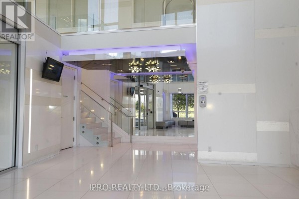Modern building lobby with white tiled floors, glass elevators, and contemporary lighting. - 409 - 110 Marine Parade Drive, Toronto