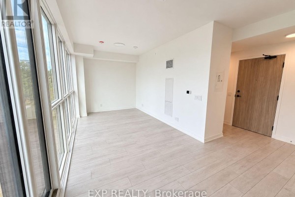 Empty living room with light wood floors, white walls, and a large window. - 409 - 1381 Lakeshore Road, Mississauga