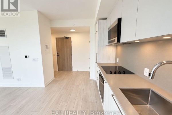 View of a modern kitchen with light wood cabinets, stainless steel appliances, and light countertops. - 409 - 1381 Lakeshore Road, Mississauga