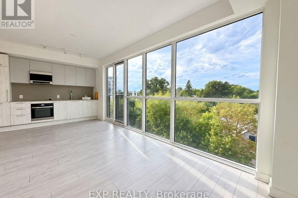 Open concept living area with a modern kitchen and large corner windows overlooking trees. - 409 - 1381 Lakeshore Road, Mississauga