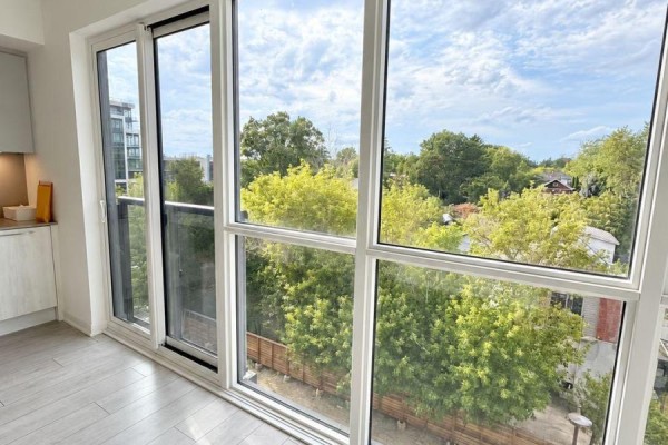 Interior view of large windows showing green trees and houses under a cloudy sky. - 409 - 1381 Lakeshore Road, Mississauga