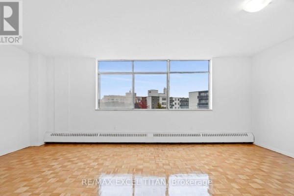 Empty room with light wood parquet flooring and a large window overlooking buildings. - 409 - 2255 Weston Road, Toronto