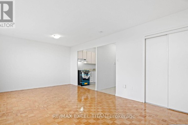 Interior view of a living area with parquet flooring, white walls, and an open doorway to a kitchen. - 409 - 2255 Weston Road, Toronto