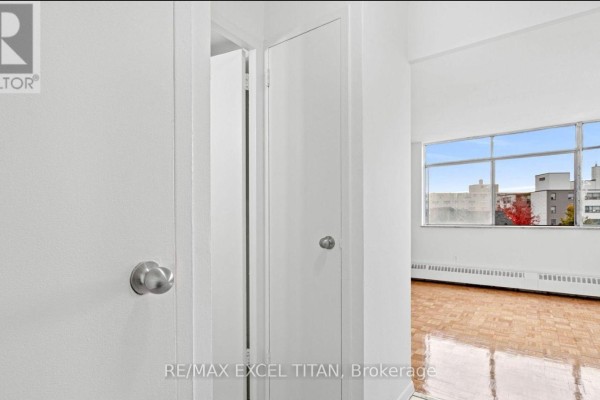 Interior hallway with white walls, a closet door, and a view into a room with a large window. - 409 - 2255 Weston Road, Toronto
