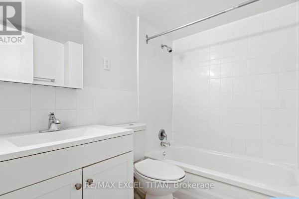 A white bathroom with a vanity, toilet, bathtub, and tiled walls. - 409 - 2255 Weston Road, Toronto