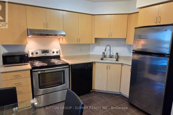 L-shaped kitchen with light wood cabinets, stainless steel appliances, and dark tiled floor. - 409 - 35 Saranac Boulevard, Toronto