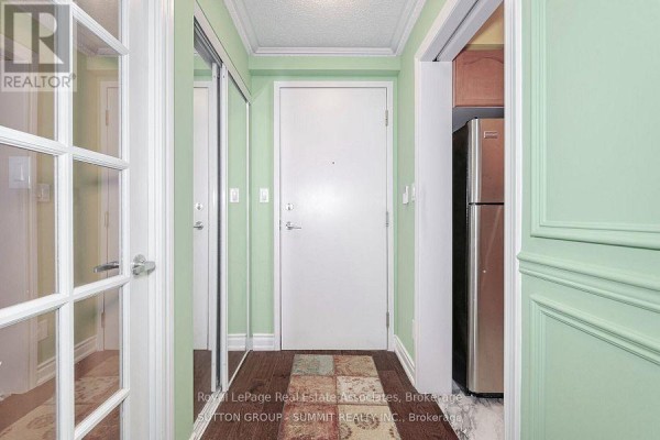 Apartment entryway with wood floors, mirrored closet doors, white door, and stainless steel refrigerator. - 409 - 3880 Duke Of York Boulevard, Mississauga