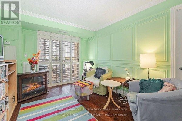 Living room with green paneled walls, furniture, electric fireplace, and sliding glass doors. - 409 - 3880 Duke Of York Boulevard, Mississauga